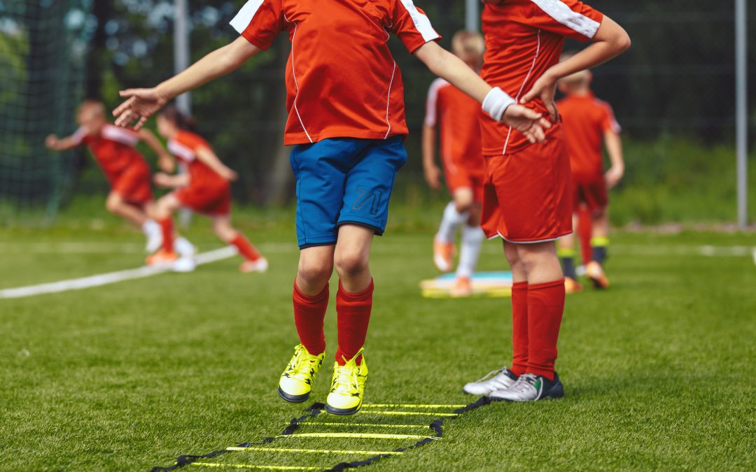 Group of children jumping over training ladder during soccer football summer camp. Boys of junior football club improving skills at a training session