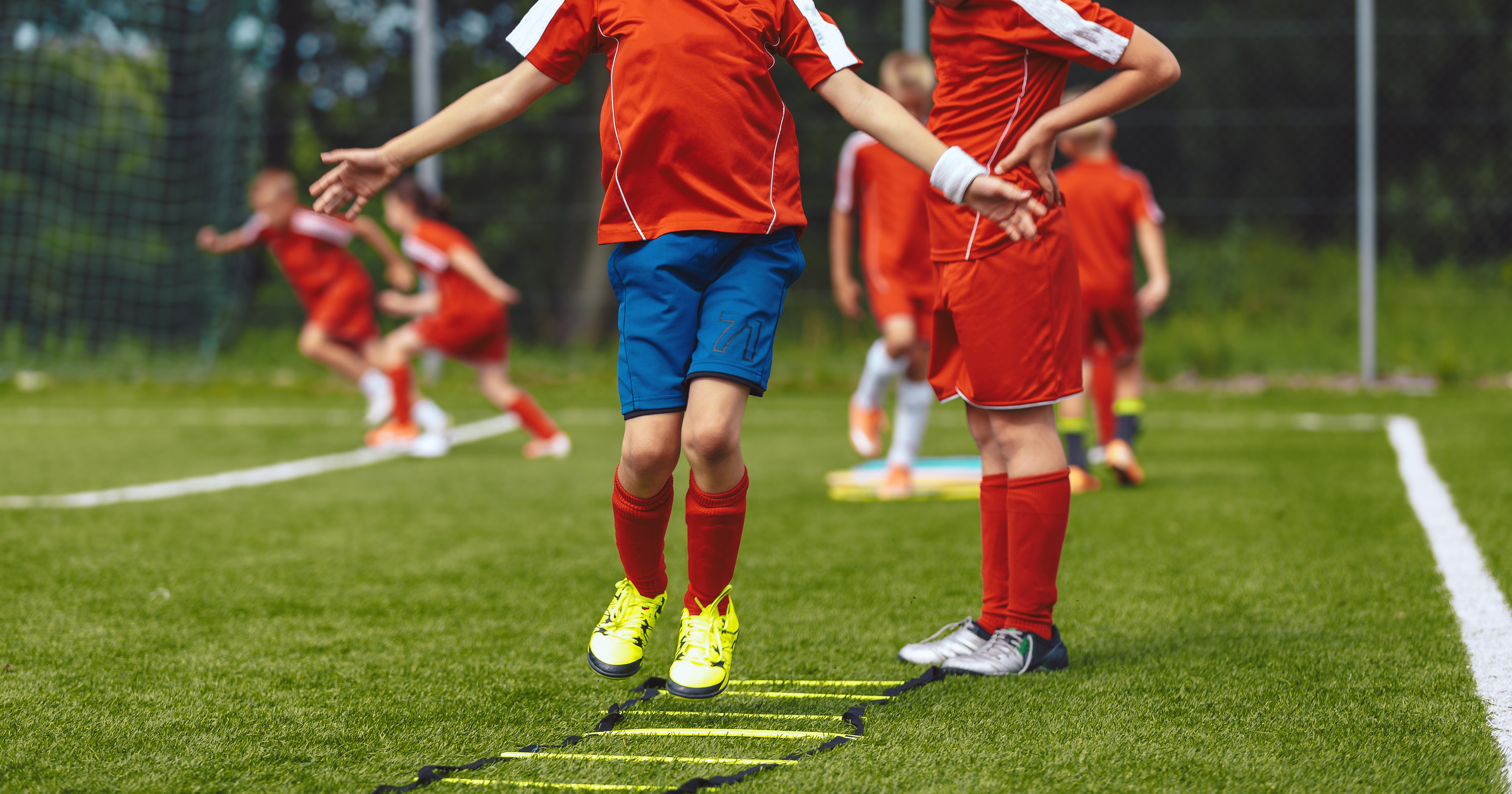Group of children jumping over training ladder during soccer football summer camp. Boys of junior football club improving skills at a training session