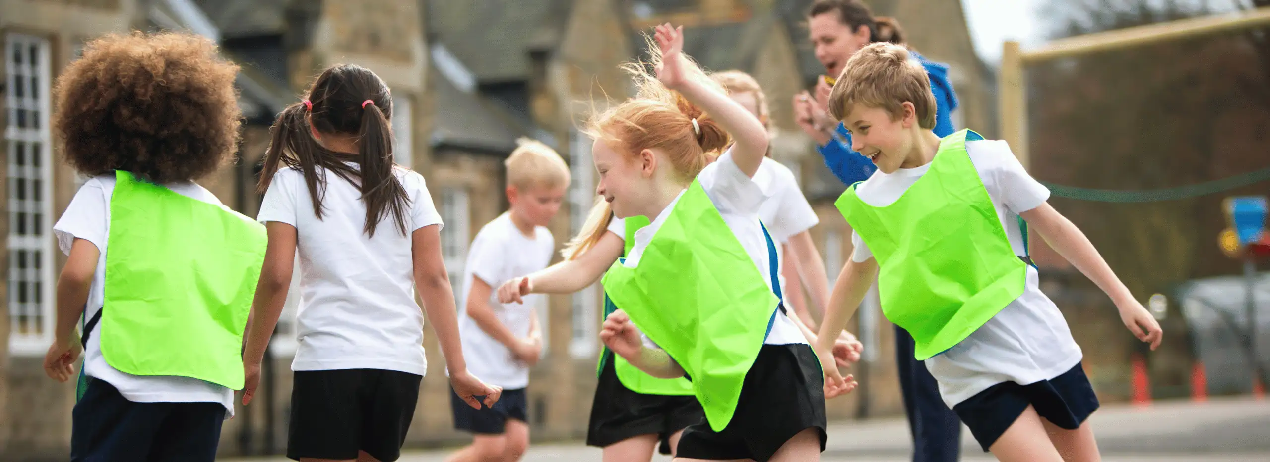 A group of children doing PE in the playground with a young apprentice