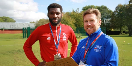 Two sports coaches stand on a pitch