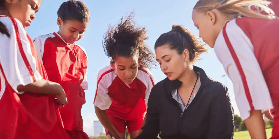 a group of children huddle round a female apprentice sports leader
