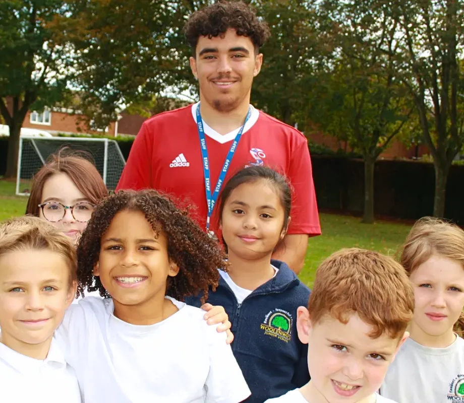 A PE Apprentice standing in a huddle with a group of children